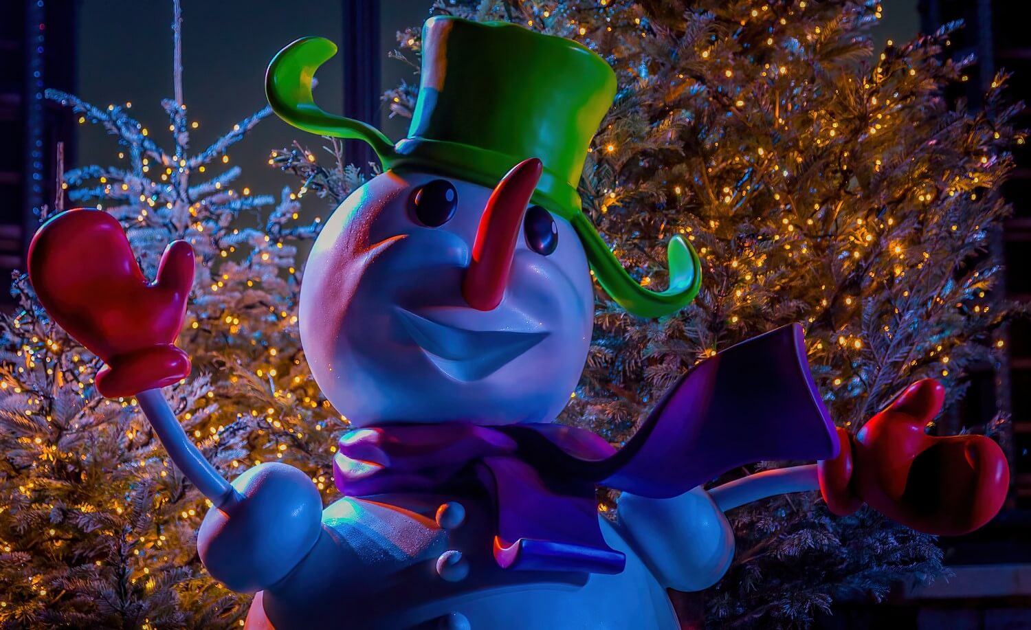 Kopf eines Schneemanns hinter dem mit verschneite Bäume stehen, die mit hunderten Lichtern beleuchtet sind