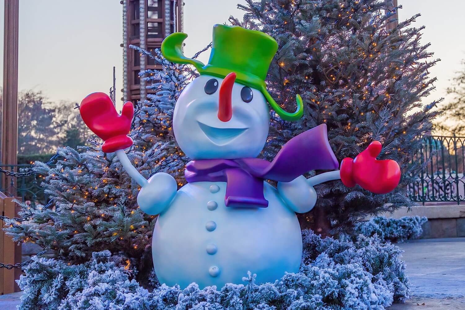 Freundlich schauender Schneemann mit grüner Mütze, lila Schal und roten Handschuhen