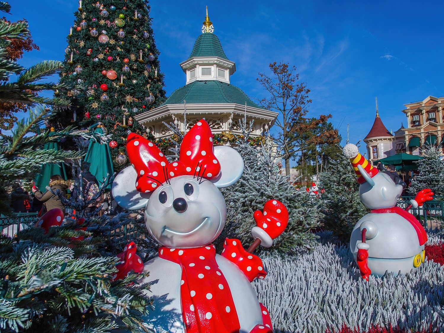 Minnie Mouse Schneemann im verschneiten Wäldchen am Town Square, im Hintergrund Gazebo und Weihnachtsbaum