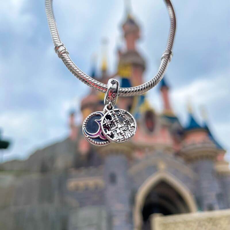Silver bracelet with two small pendants. One pendant shows the silhoutte of the castle, the other a pink 30 on a blue background