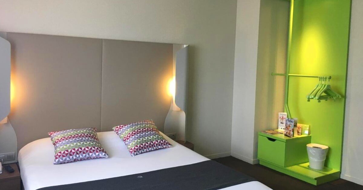 Doppelzimmer mit einer quietschgrünen Gaderobe und bunt gemusterten Zierkissen auf dem Bett
